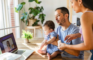 Parents with their baby having an online consultation with a doctor through a video call on a laptop at home