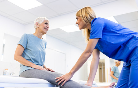 Female physiotherapist helping an elderly woman with a leg exercise during a rehabilitation session in a clinic