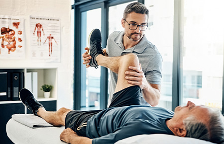 Physiotherapist assisting an elderly man with leg exercise