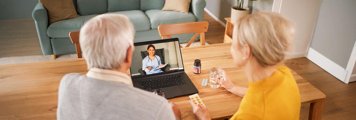 An elderly couple having an online medical consultation with a doctor on a laptop at home.